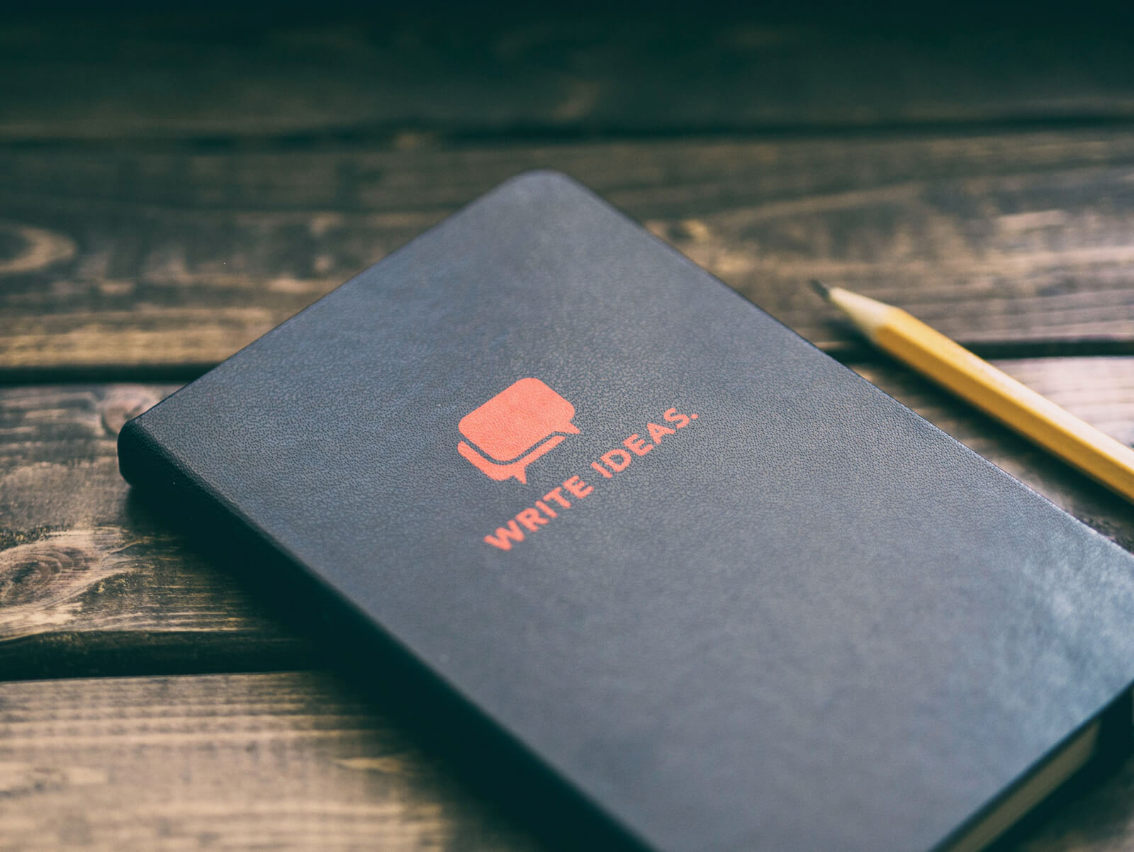 A notebook reading "Write ideas" with a pencil beside it on a wooden desk