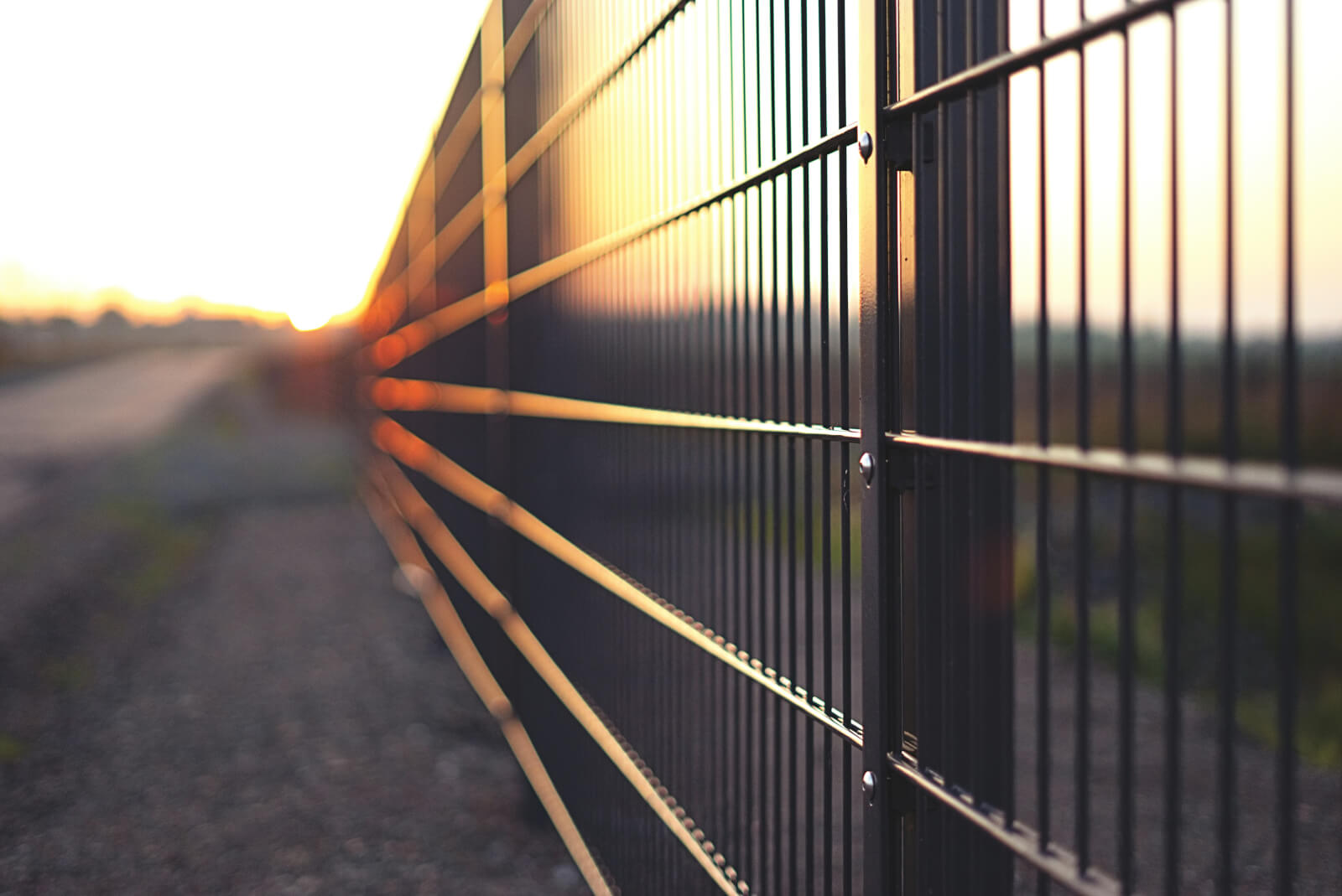A dark metal fence running along a gravel path at sunset