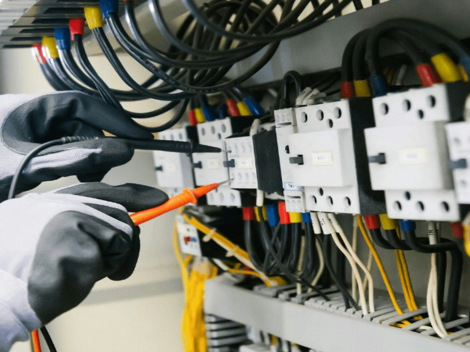 Electrician in work gloves testing a breaker panel with a multimeter